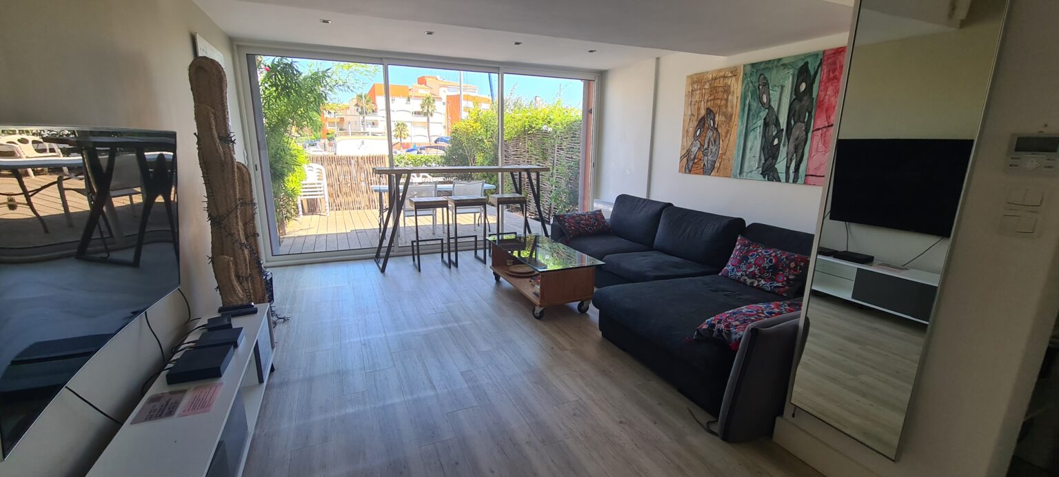 Photographie du salon de la villa, avec son grand canapé, sa télévision et ses tables bar